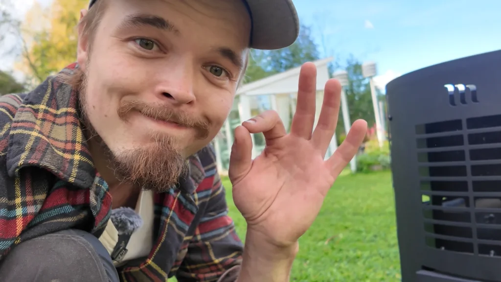 Puulate hymyilee pihalla kiukaan vieressä ja näyttää ok-merkkiä.